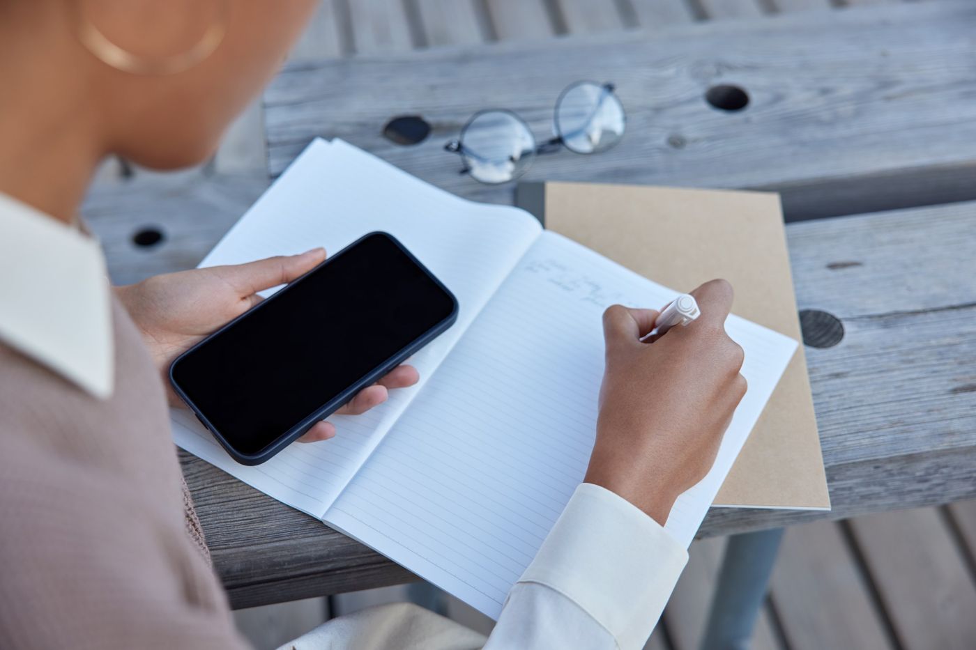 Manos tomando notas en un cuaderno junto a un teléfono