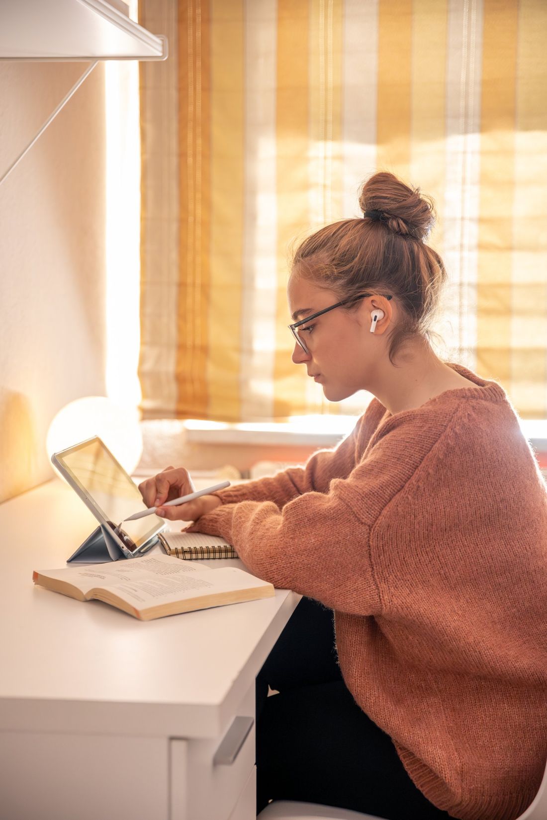 Mujer escribiendo con un lápiz digital en una tablet, junto a un libro abierto